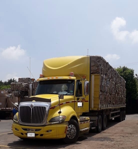 Tracto camión amarillo encendido de noche con luces brillantes, listo para el transporte de materiales reciclables. Un pilar fundamental en la logística del Nuevo Mundo del Reciclaje, impulsando una movilidad sostenible y eficiente.